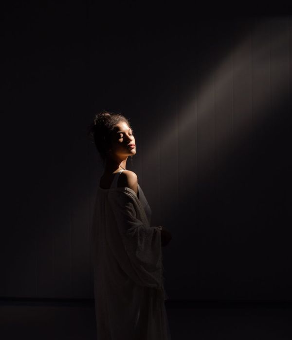 Woman in a graceful wellness pose in a dark room with honey-colored light.